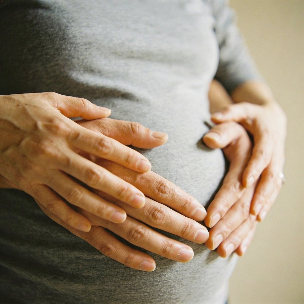 Hände von Mutter und Vater formen ein Herz auf dem runden Schwangerbauch